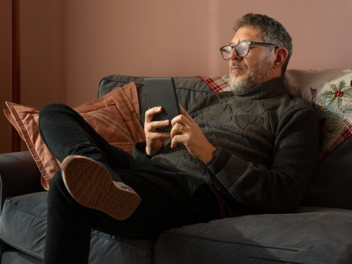 A man is sitting on a couch with an ebook reader in his hand